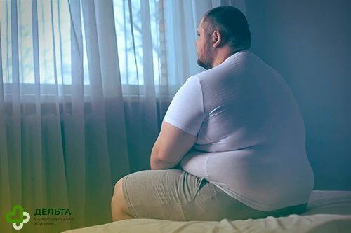 Мужчина с ожирением сидит на кровати